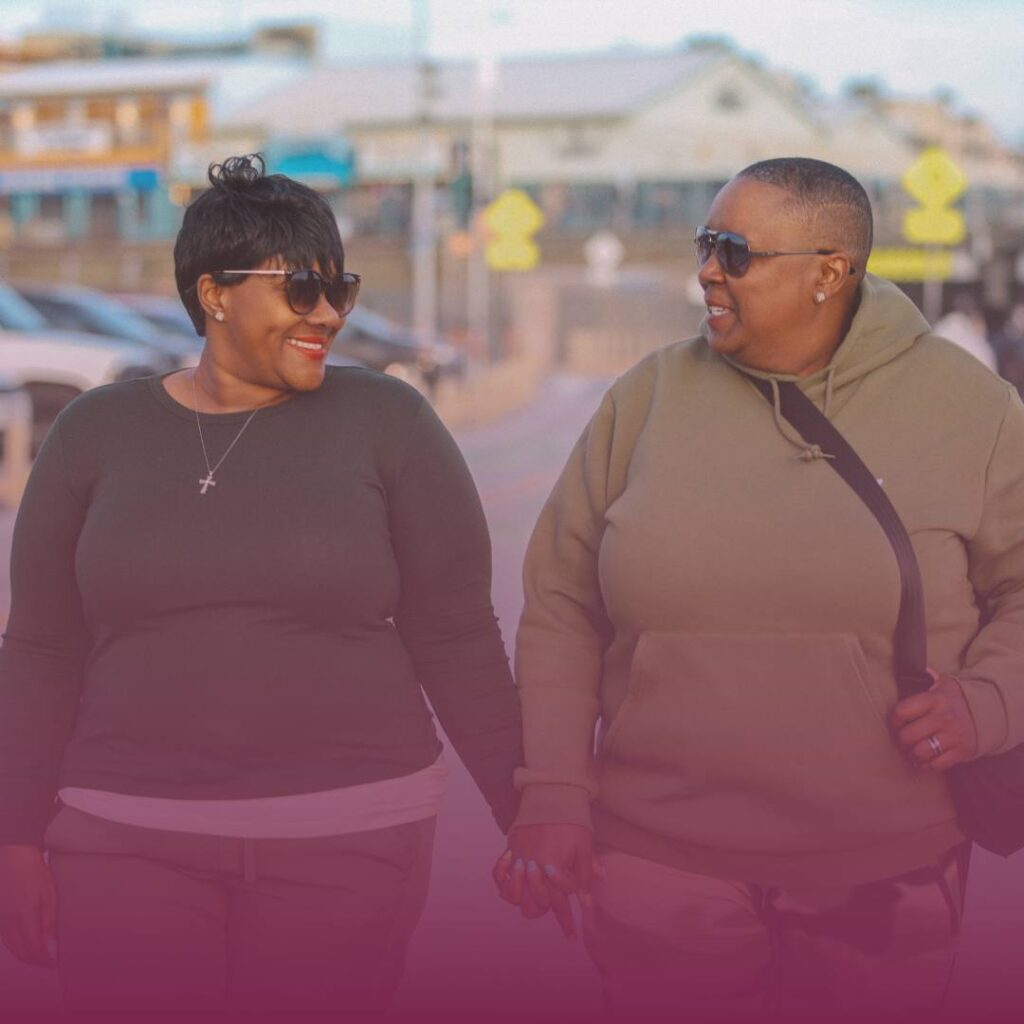 Proud black lesbian couple holding hands and looking at eachother smiling while walking down the street